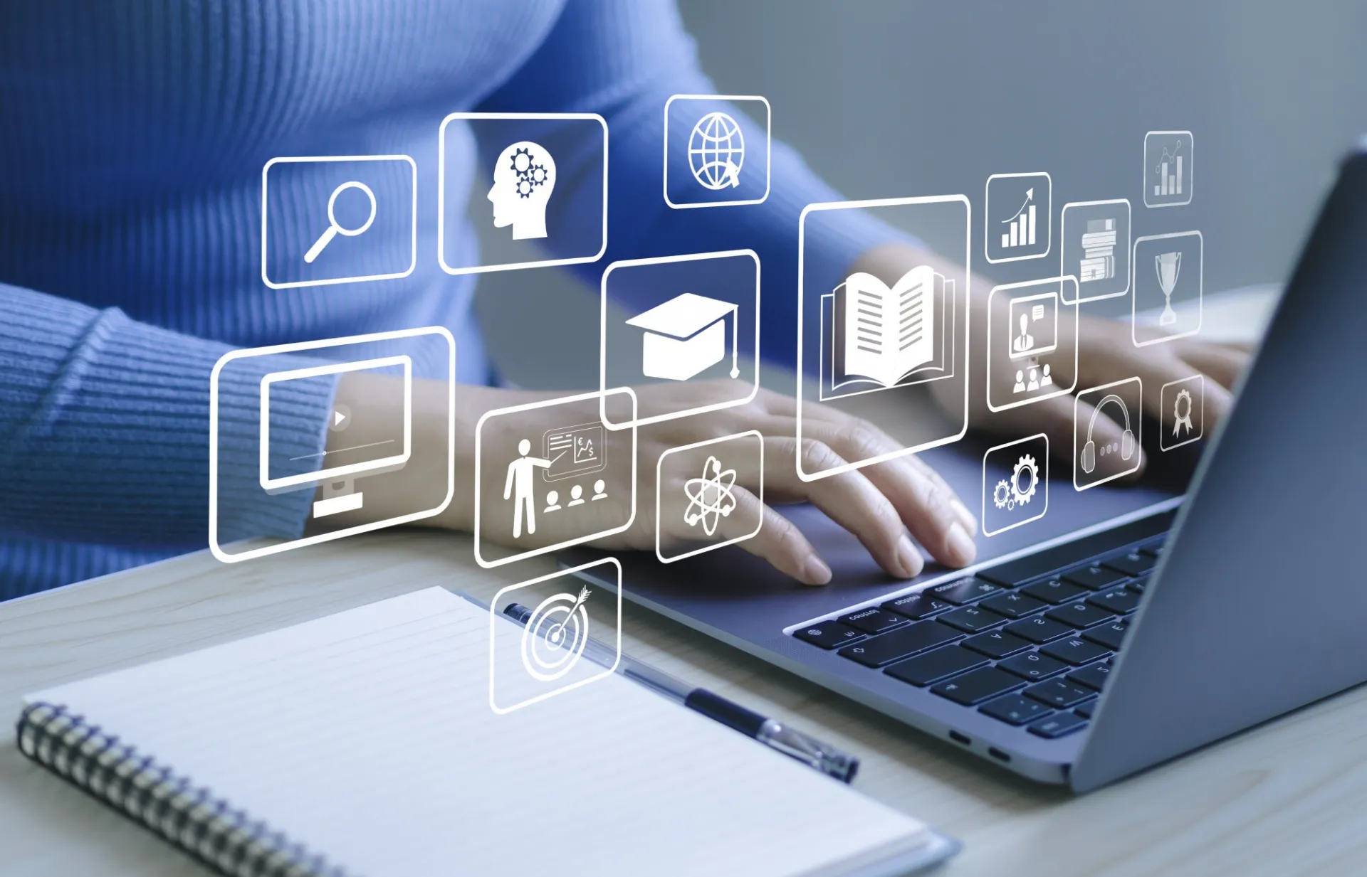 Woman's hands typing on a laptop while educational icons hover around her hands. 